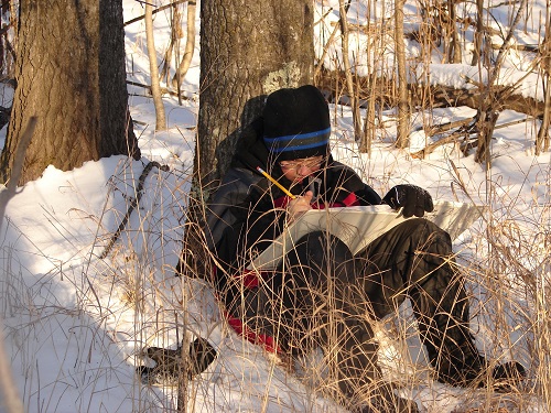 student-sitting-against-tree-in-snow-writing-poetry