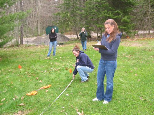 A pair of students measures and marks their forest plot with a small orange flag. 