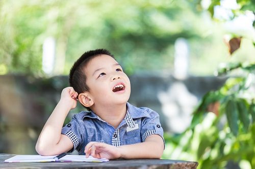 young-boy-sitting-at-table-outdoors-with-exercise-book