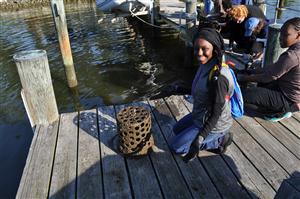 Student sitting on a dock with a barrel of oysters