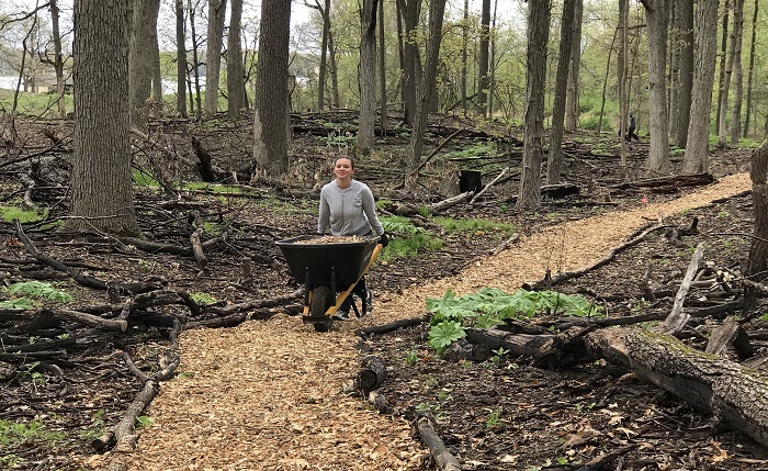 girl-pushes-wheelbarrow-woodchips-forest-hiking-trail