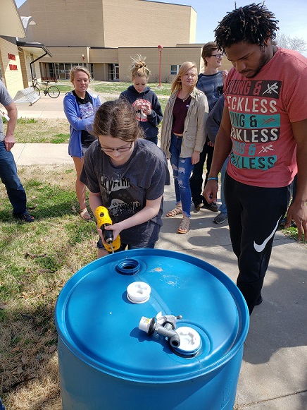 students drill holes into a rain barrel
