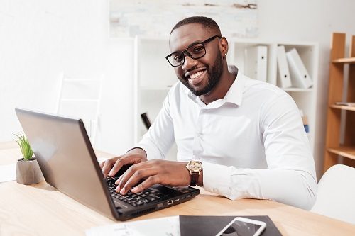 Portrait of smiling african american businessman in white shirt working on his laptop in office 