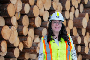 Female logger standing in front of stacked logs