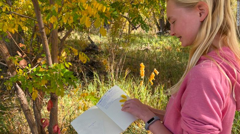 A student writes in her nature journal outdoors.