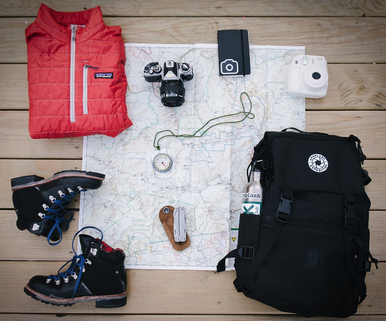 overhead-photo-of-backpack-boots-cameras-map-jacket-and-compass