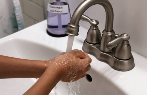 young person washes their hands under a faucet
