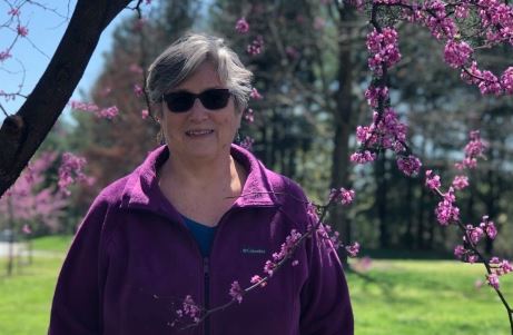 photo of page hutchinson in a purple fleece standing before a bright pink redbud tree