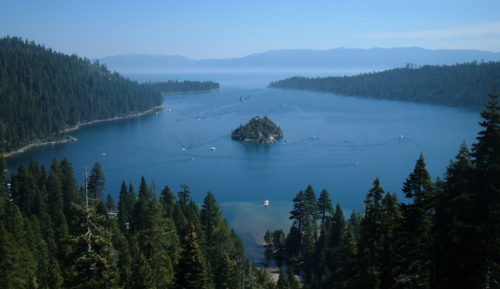 photo of emerald bay a small forested island sits nestled in a evergreen forested half circle of land surrounding a bright blue bay