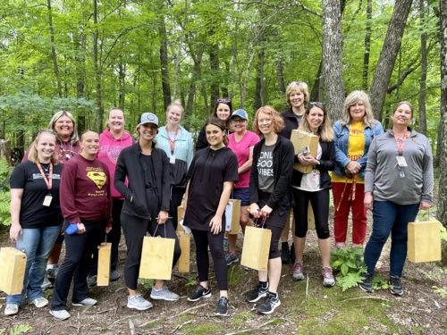 a group of educators stand in the woods holding lightweight portable wooden desks and smile for the photodesks