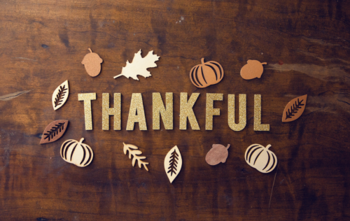 wood background with glitter letters cut our spelling thankful