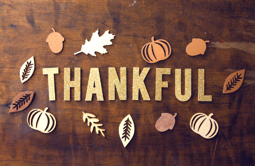 wood background with glitter letters cut our spelling thankful