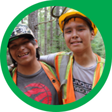 young indigenous men in orange safety vests and hardhats hug in a forest