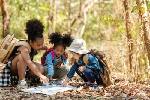 Three children kneeling around a map in the forest during fall