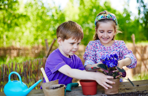 a young boy and girl working together to pot a purple flower