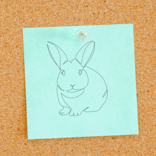green sticky note with a drawing of a bunny attached to a cork board