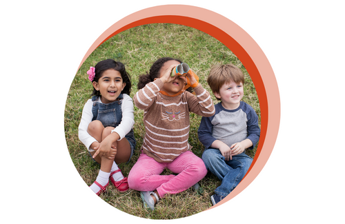 3 young kids sitting on a grassy hill looking into cardboard binoculars