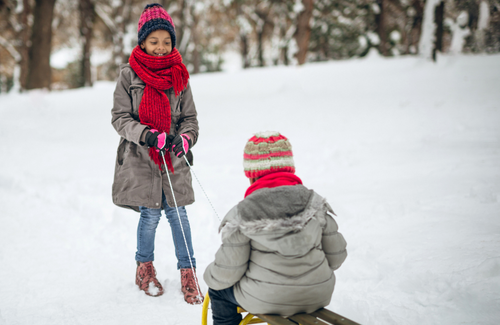 young girl pulling child on sled through the snow